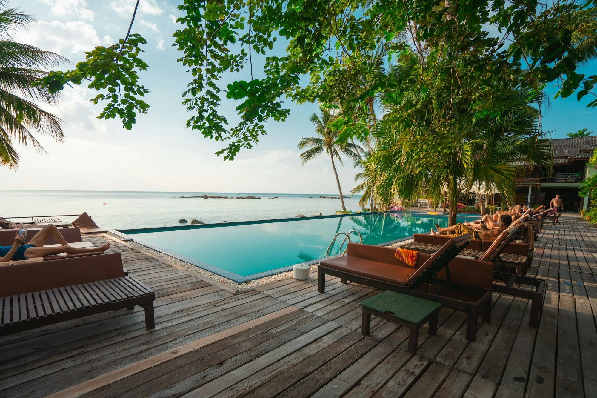 A wooden deck with loungers beside an infinity pool facing the sea